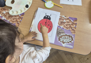 dziewczynka stempluje paluszkiem czarną kropkę na biedronce
