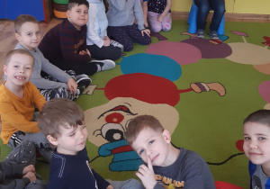 12 cioro dzieci siedzi w półkolu, jeden chłopiec trzyma torbę z cukierkami
