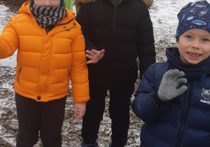 Na pierwszym planie widać 3 chłopcó machających ręką za nimi widać zaśnieżone urządzenia terenowe