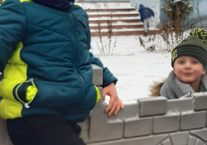 Na pierwszym planie widać 2 chłopców bawiących się w zamku, na drugim planie widać chłopca wchodzącego po schodach