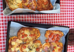 na stole przykrytym obrusem w kratę leżą dwie blachy na których są upieczone pizze