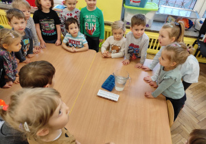 Na stolikach stoją kostkarki do lodu i woda w dzbanku. Wokół stolików stoją dzieci
