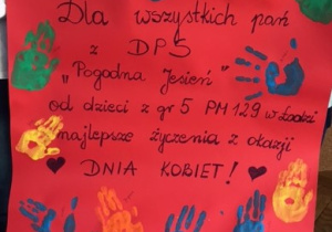 Laurka z życzeniami w kolorze czerwonym. Na niej odbite dłonie wszystkich dzieci z grupy.