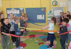 Dzieci tańczą na dywanie i trzymają w dłoniach kolorową bibułę.