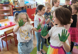 Dzieci stoją na dywanie pokazując dłonie pomalowane farbami.