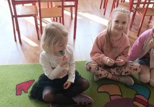 Dzieci siedzą na dywanie i degustują szpinak.