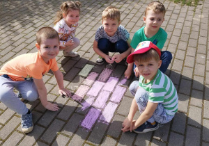 Dzieci w parku na chodniku rysują kredą.