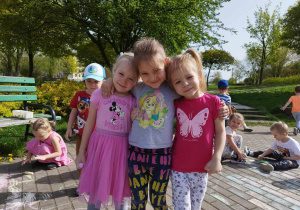 Trzy dziewczynki w parku trzymają się za ramiona.