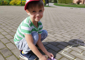 Chłopiec w parku na chodniku rysuje kredą .