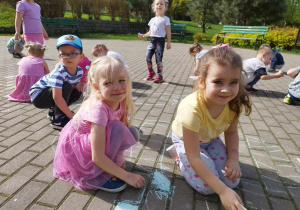 Dziewczynki w parku na chodniku rysują kredą.