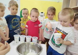 Dzieci oglądają jak chłopiec przekłada łyżką jogurt do miski.
