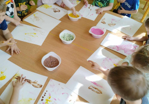 Dzieci przy stole malują jadalnymi farbami.