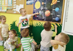 Chłopiec wskazuje dzieciom na tablicy demonstracyjnej planetę ziemię.
