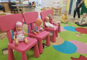 Na czterech różowych krzesłach siedzą lalki.