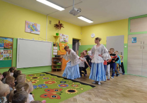 Dzieci stoją w dwóch rzędach za tancerkami.