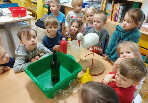Dzieci stoją wkoło stolika z figurką bociana i materiałami do zabawy badawczej.