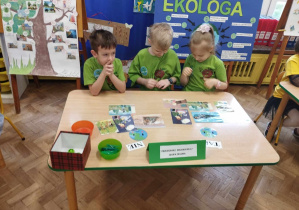 3 dzieci w zielonych koszulkach wykonują zadanie przy stole