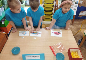 Dzieci w niebieskich koszulkach układają puzzle przy stole