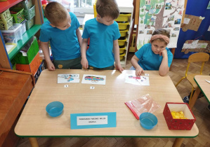 Dzieci w niebieskich koszulkach układają puzzle przy stole
