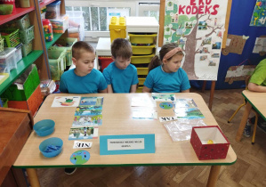 3 dzieci w niebieskich koszulkach wykonują zadanie przy stole