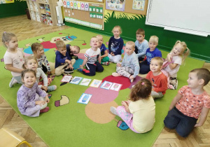 Dzieci siedzą na dywanie i oglądają obrazki z środkami higienicznymi.