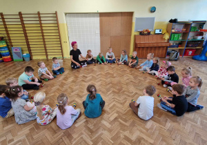 Dzieci siedzą w kole i grają z instruktorem na grzechotkach