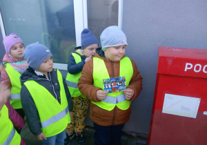 Dzieci stoją przy skrzynce pocztowej jeden chłopiec trzyma kartkę