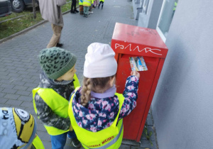 Dzieci wrzucają kartkę pocztową do skrzynki na listy.