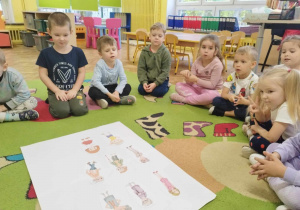 Dzieci oglądają obrazki z wizerunkami ludzi, które są rozłożone na białym arkuszu papieru.