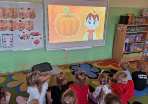 Dzieci siedzą na dywanie i oglądają film edukacyjny o dyni