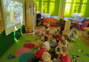 Dzieci oglądają film edukacyjny na tablicy multimedialnej.