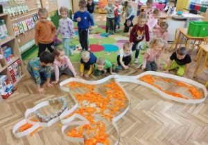 Dzieci rozdmuchują kawałki pociętej, pomarańczowej bibuły w szablonie wiewiórki.