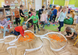 Dzieci ozdabiają szablon wiewiórki pocięta, pomarańczową bibułą.