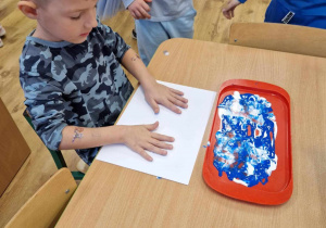 Chłopiec macza dłonie w niebieskiej farbie.