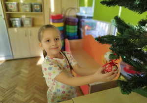 Dziewczynka zawiesza bombkę na choinkę.