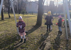 Dzieci bujają się na huśtawce w ogrodzie.