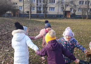 Dzieci śpiewają i tańczą w kole w ogrodzie.