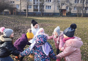 Dzieci śpiewają i tańczą w kole w ogrodzie.