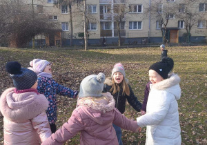 Dzieci śpiewają i tańczą w kole w ogrodzie.