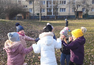 Dzieci śpiewają i tańczą w kole w ogrodzie.