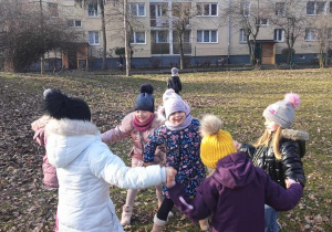 Dzieci śpiewają i tańczą w kole w ogrodzie.