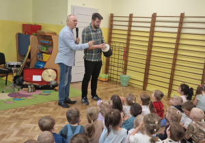 Dwóch mężczyzn pokazuje dzieciom instrument