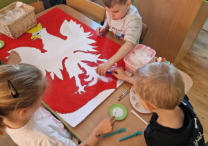 Dzieci przyklejają białe pióra na sylwete orła