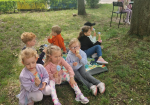 Dzieci siedzą na macie piknikowej i jedzą lody