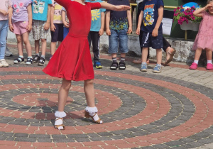 Dziewczynka w czerwonej sukience tańczy na pikniku