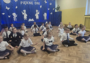 Dzieci w galowych stroach siedzą na podłodze