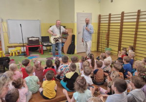 Pan z mikrofonem przedstawia Pana grającego na gitarze basowej