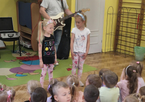 Dwie dziewczynki słuchają jak pan gra na gitarza