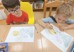 Dzieci siedzą przy stole i kolorują świetliki.