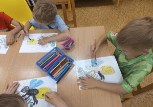 Dzieci siedzą przy stole i kolorują świetliki.